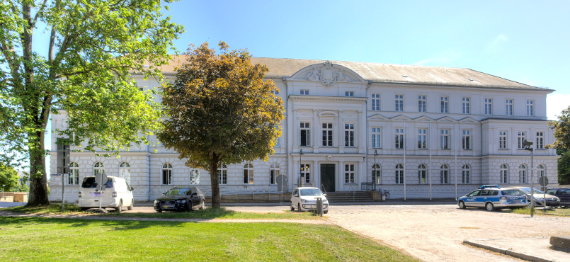 Das Gerichtsgebäude in weiss des Amtsgericht Güstrow mit einer grünen Baumgruppe