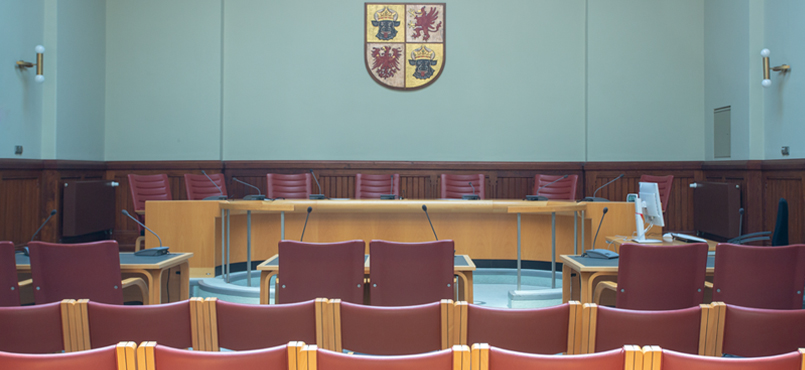 Sitzungssaal mit Blick auf das Richterpodium und dem Landeswappen an der Wand